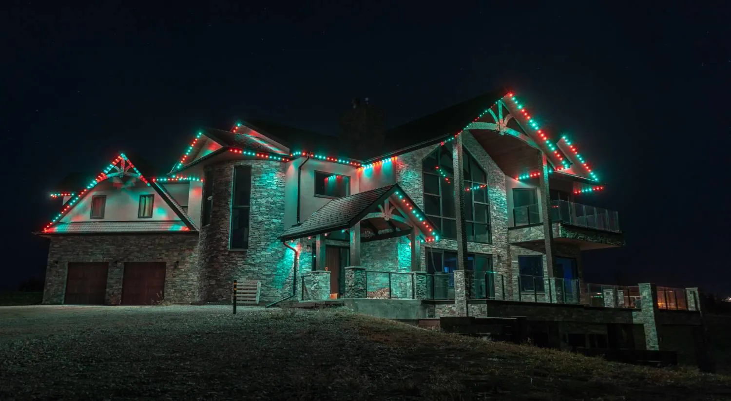 Two-story home with its rooflines lit in teal and red permanent lights at night