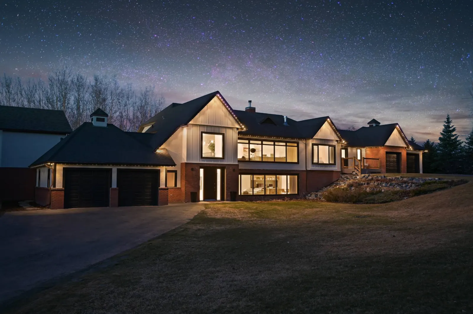 Hillside home outlined in warm white roofline lights at dusk