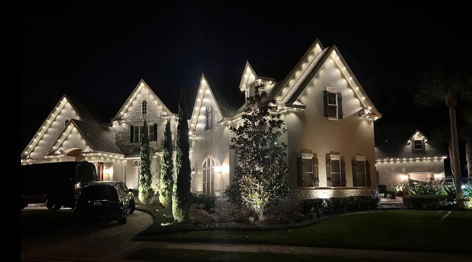 Large two-story home with warm white lights along every gable and eave, framed by a dark night sky