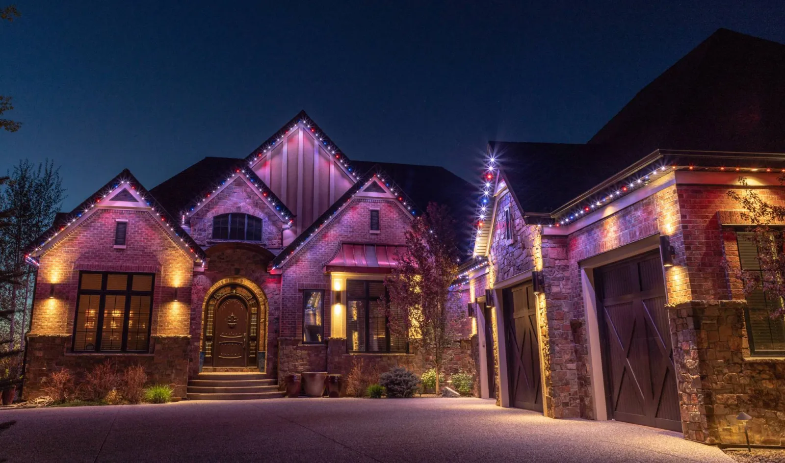 Brick home with pink and purple holiday lights along its gables at night