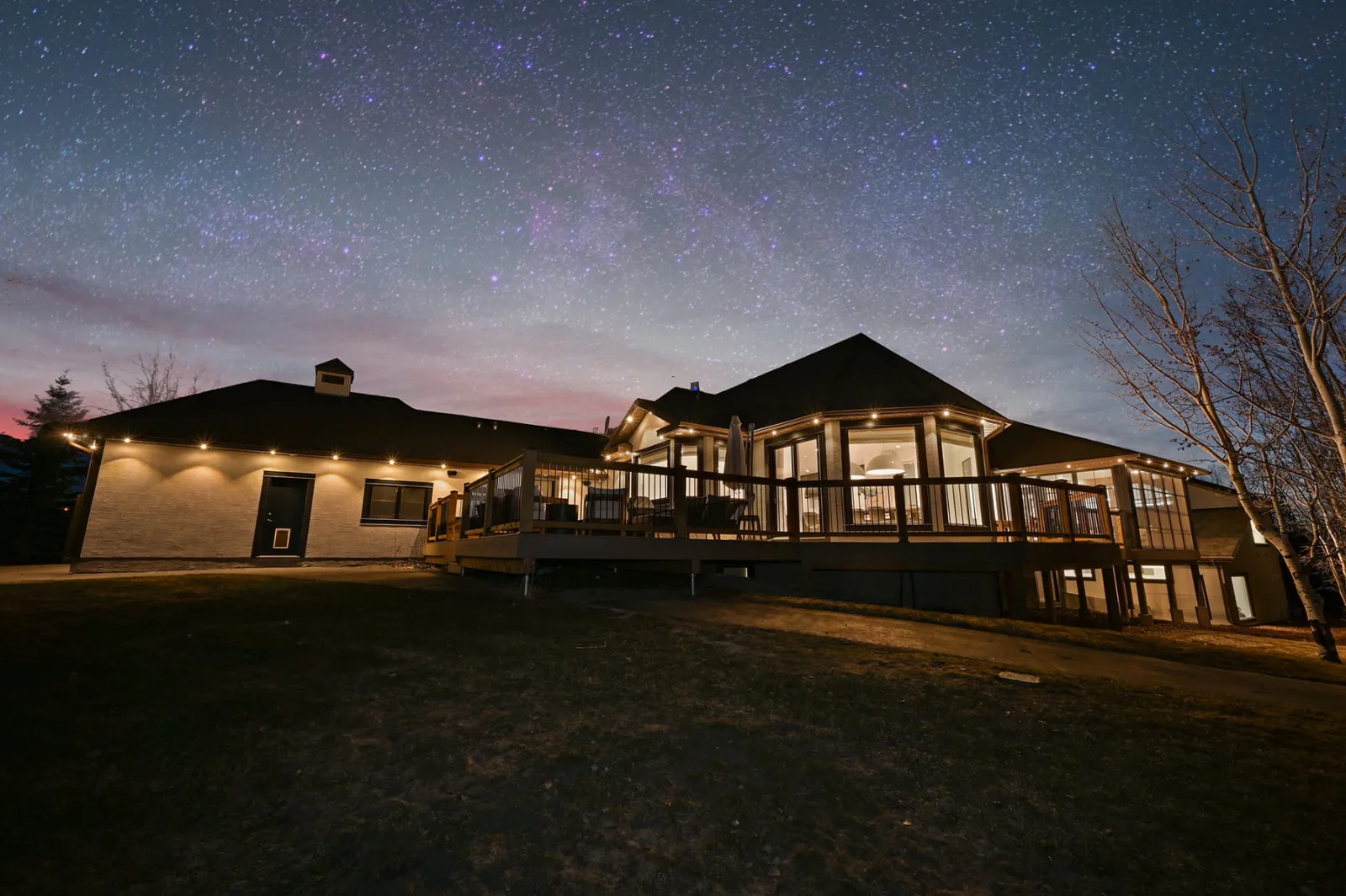 Ranch home and deck with warm white lights glowing under a starry evening sky