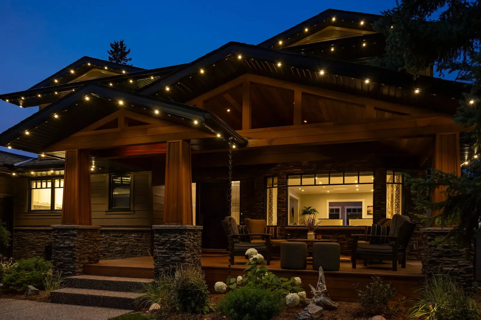 Craftsman home with warm white lights along its layered gables and covered porch at night