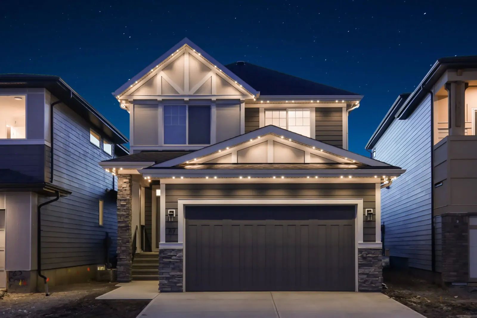 The same home at dusk with white lights along its gables, eaves and garage