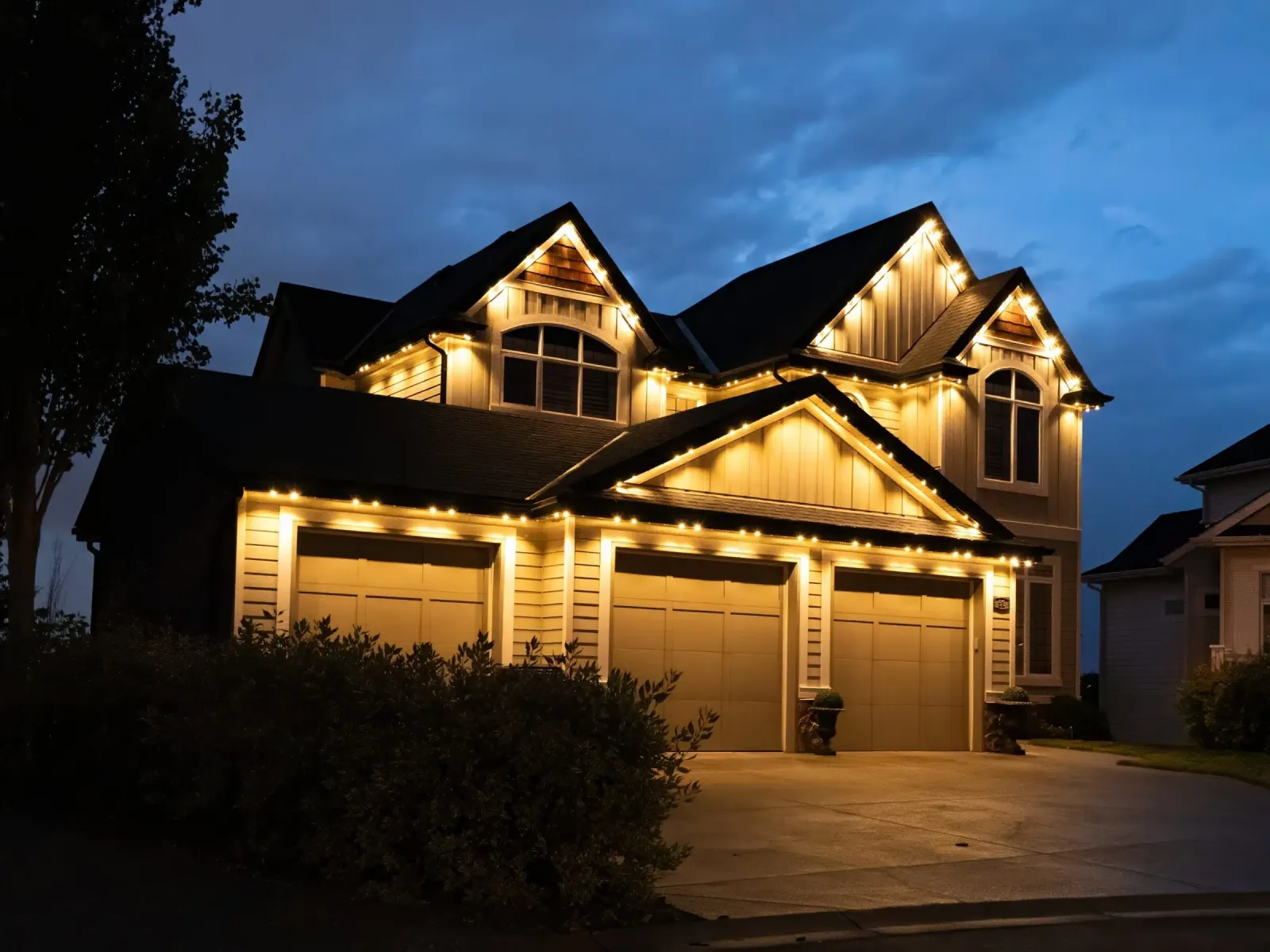 Two-story home with warm white lights along its gables and garage at dusk