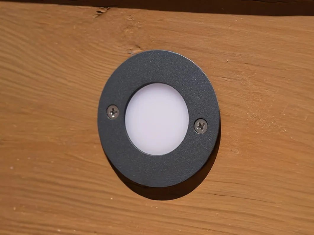 Close-up of a deck light set flush in a wood board, framed by a dark metal deck ring