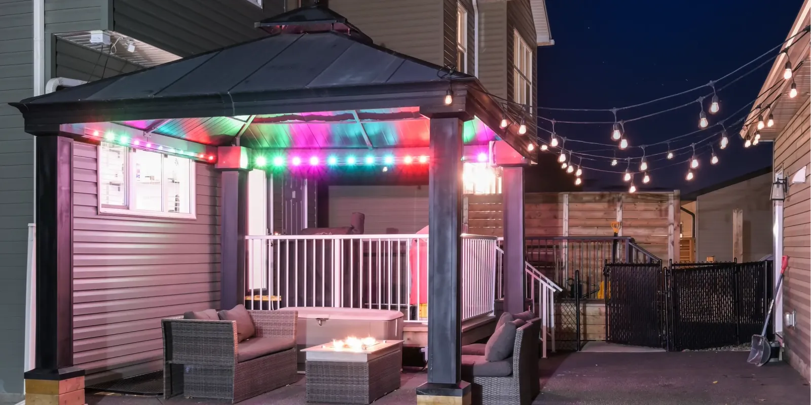 Backyard gazebo trimmed with colored lights beside patio string lights