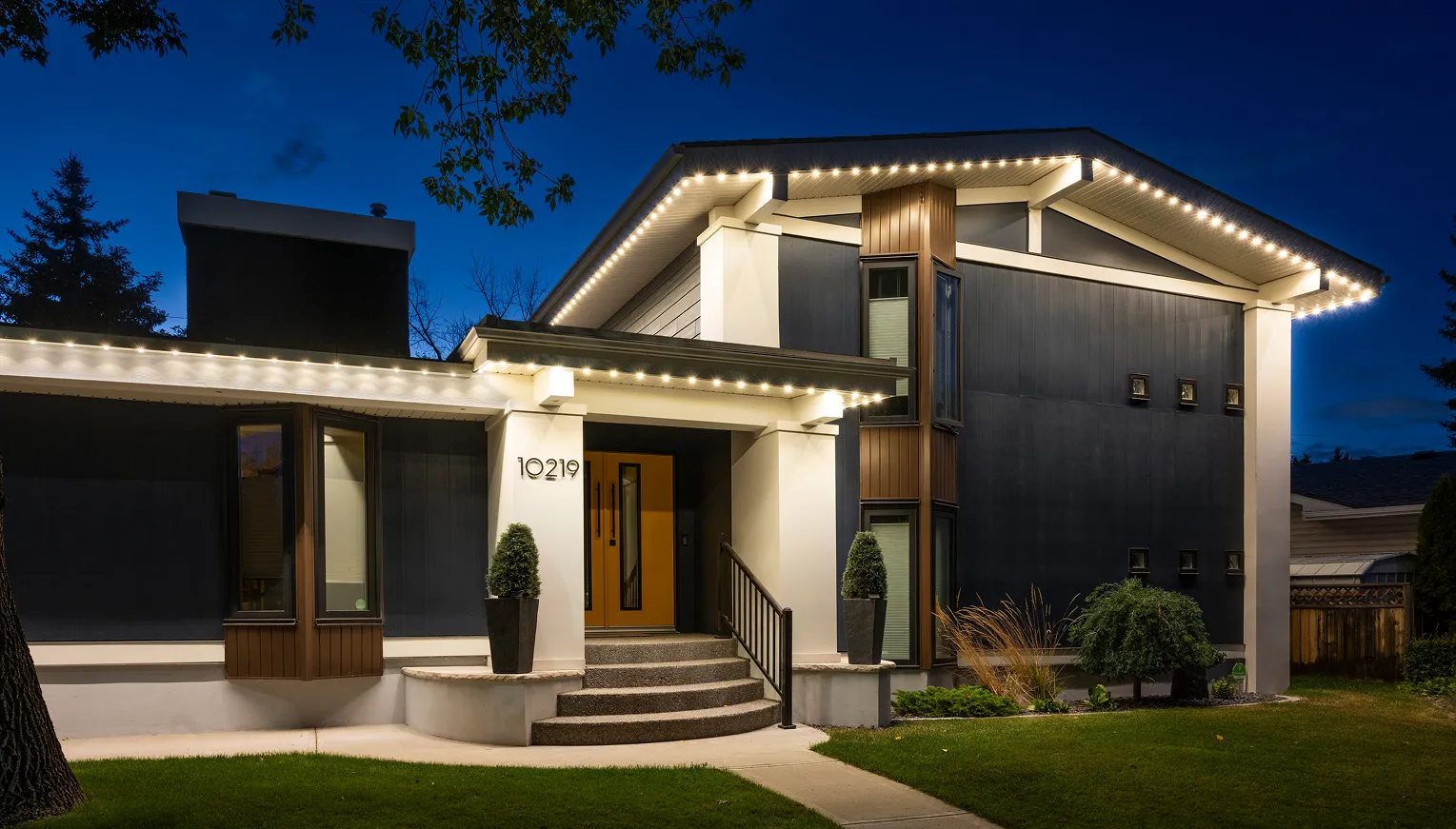 Modern home at dusk with warm white permanent lights along its rooflines