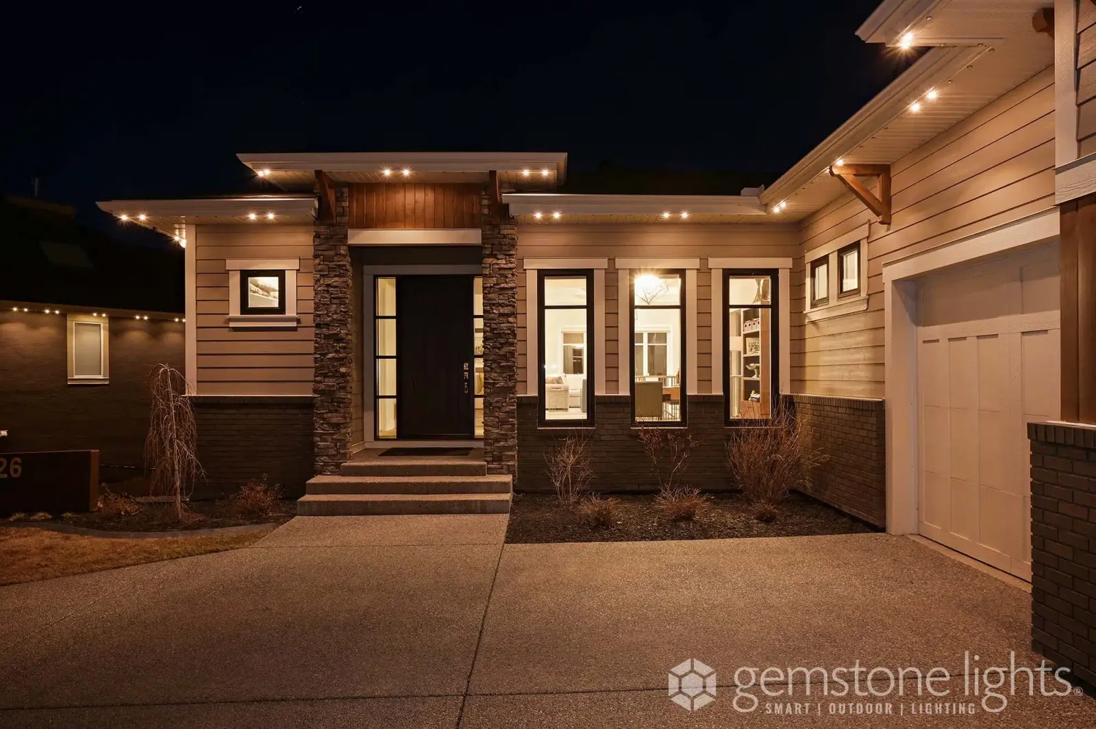 Modern home entrance with a lit front path, warm white soffit lights and a glowing double door at night