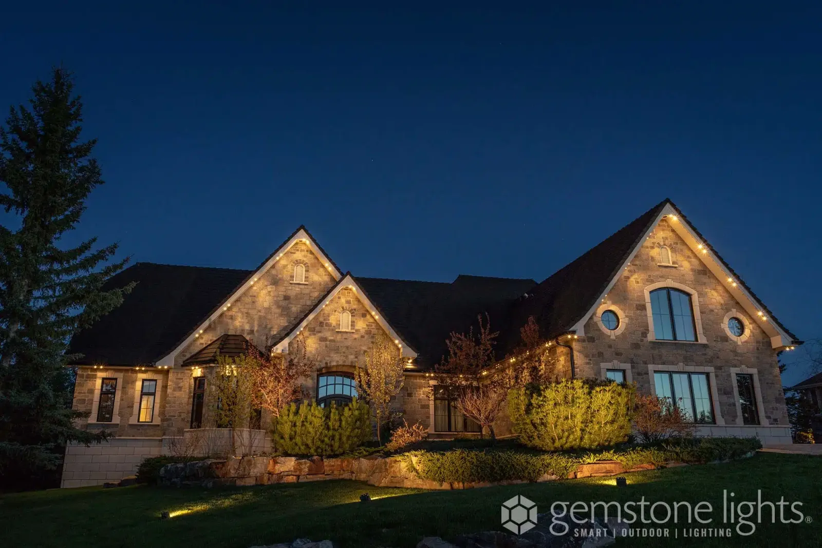Stone home with roofline and landscape lighting