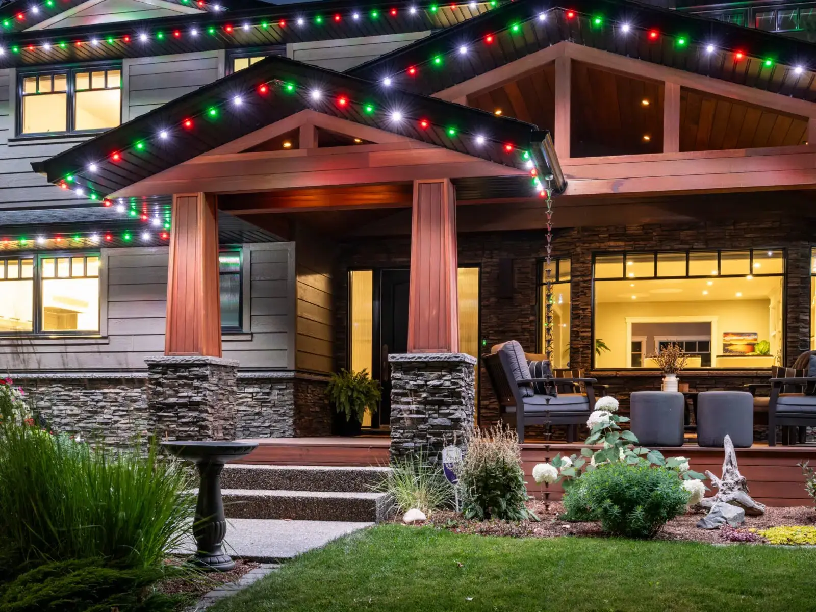 Craftsman home with a covered porch and its eaves lit in multicolor red, green and white lights